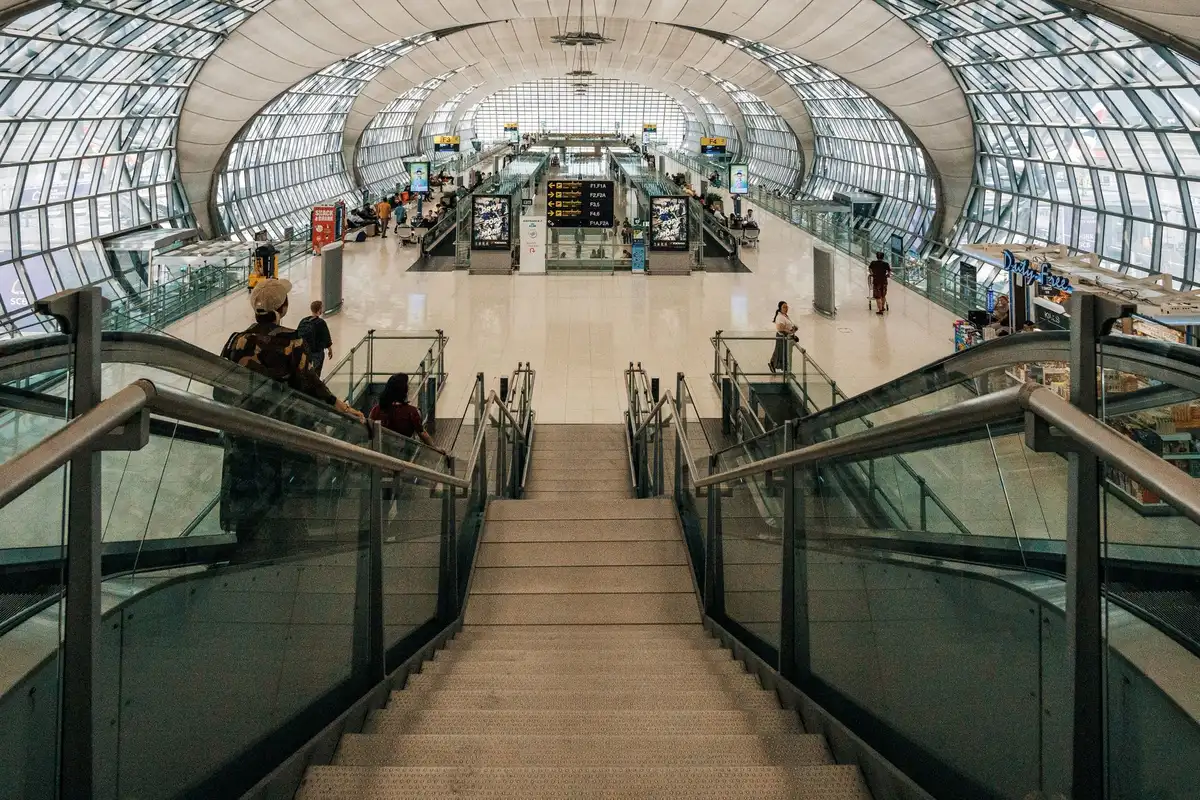Passeggeri in movimento nel terminal aeroportuale con pannelli informativi e porte d'imbarco visibili