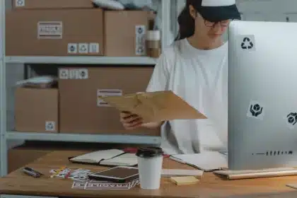 Mani che tengono documenti di spedizione e tablet digitale su scrivania di magazzino logistico