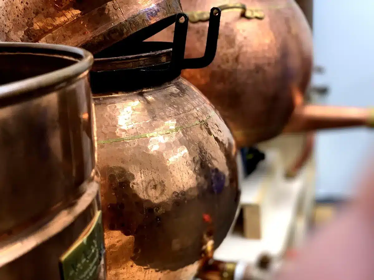 Bottiglia di gin verde con manico e attrezzature di rame per la distillazione tradizionale