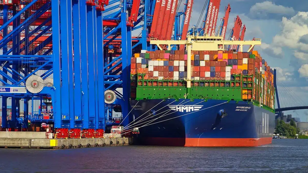 Container impilati in porto con operazioni di carico e camion in attesa