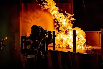 Colonna di fumo scuro sopra un impianto di rifiuti con vigili del fuoco in lontananza
