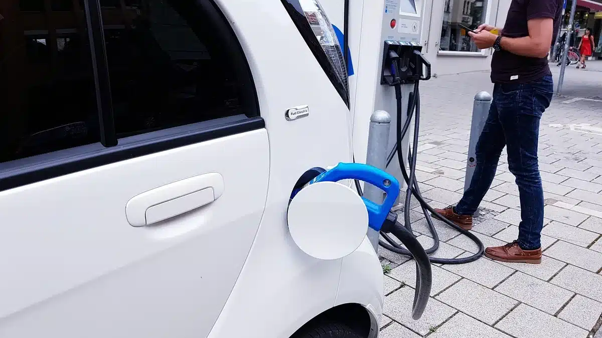 Coppia osserva auto ibride parcheggiate vicino a una colonnina di ricarica