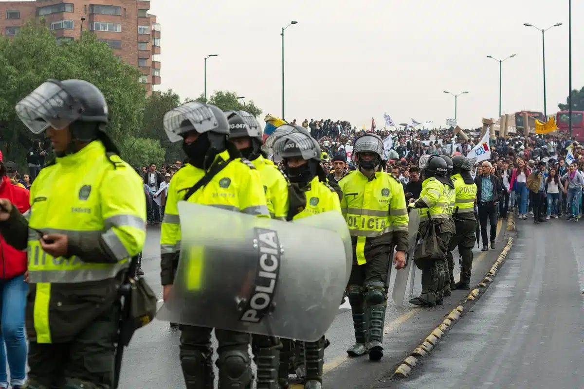Manifestanti anonimi in marcia lungo una strada provinciale con transenne e terreno smosso