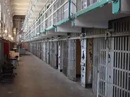 Corridoio di carcere vuoto con porte celle e figura anonima sullo sfondo